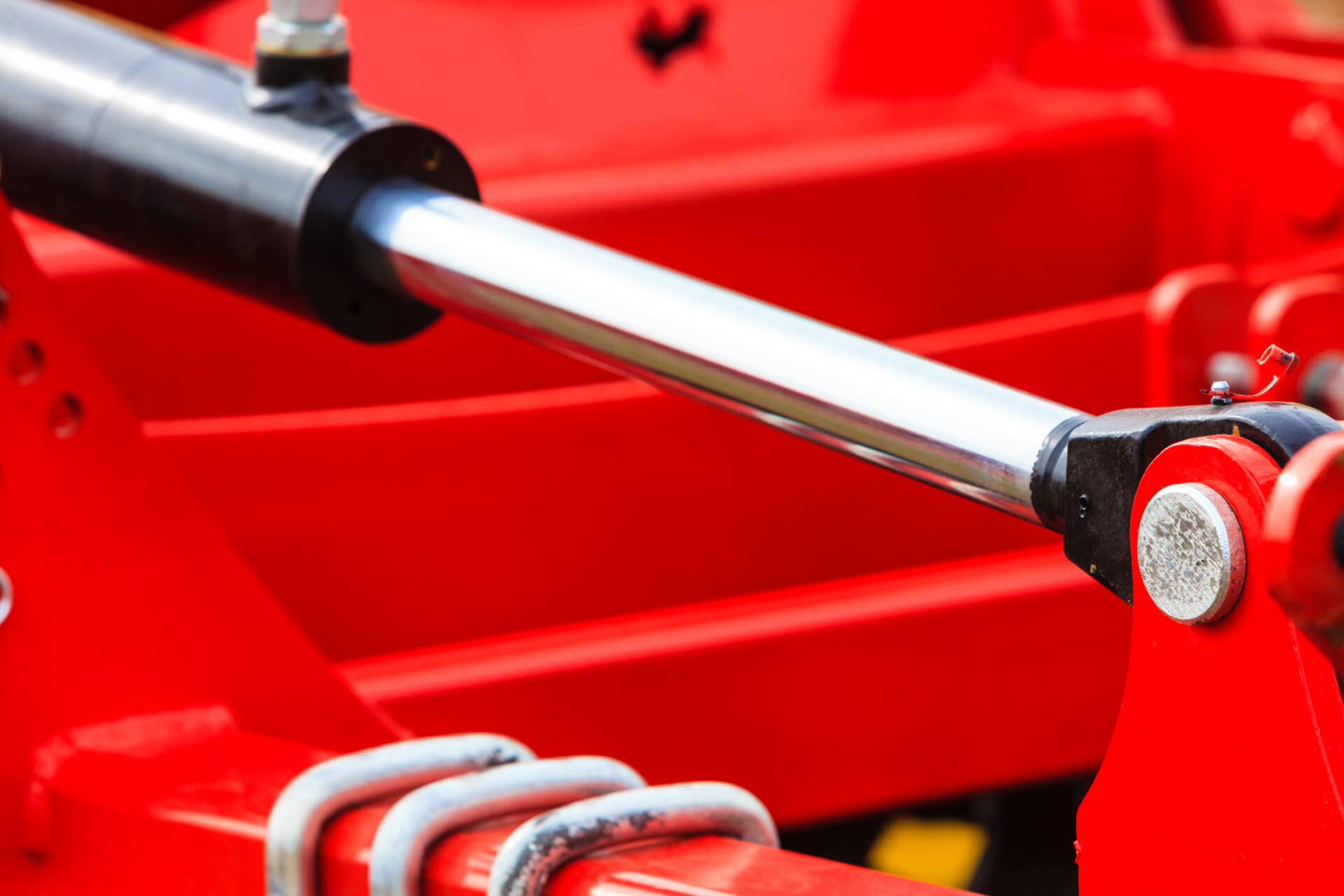 Close-up of a shiny hydraulic piston rod connected to red industrial machinery.