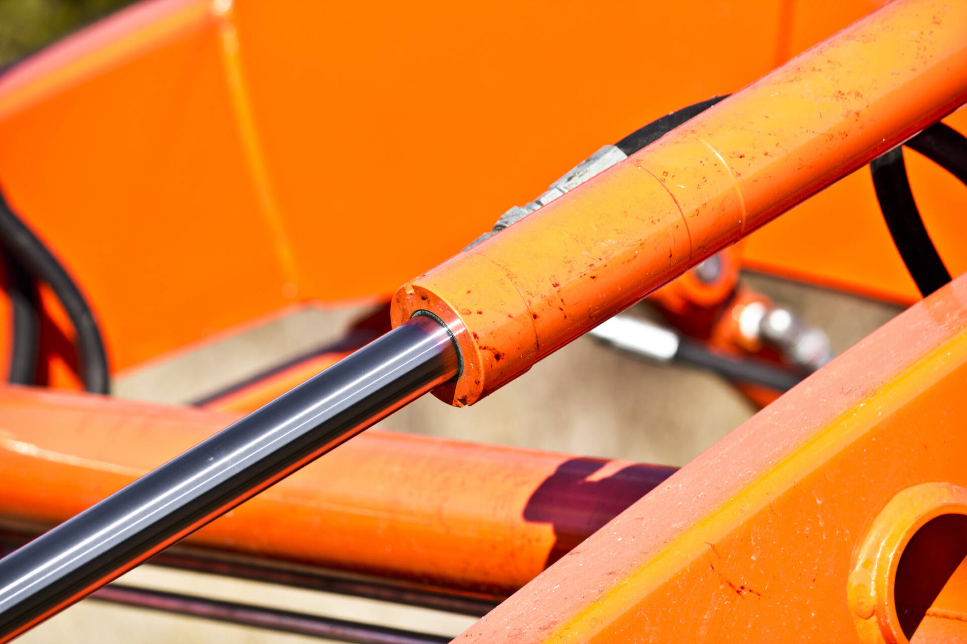 Close-up of an orange hydraulic piston rod and frame on industrial machinery.
